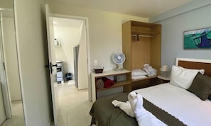 Una habitación de hotel con una cama, un ventilador, un estante con toallas y un cuadro en la pared.