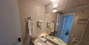A bathroom with a double sink, towel racks, a hairdryer, and a toilet visible in the background. - Marupiara Suites (Ipojuca)