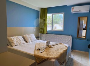 Ein Hotelzimmer mit Bett, Vorhängen an einem Fenster, einer Klimaanlage und einem Spiegel an der Wand.
