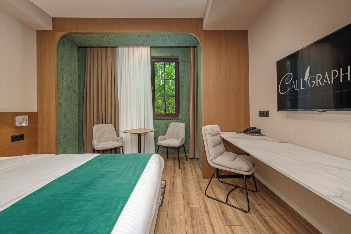 A hotel room with a bed, two chairs, a desk, and a large window with curtains.