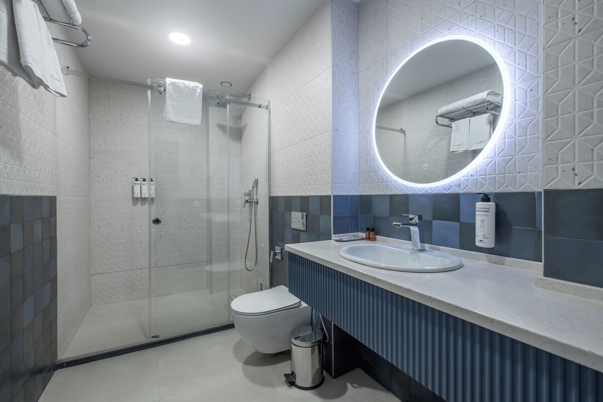 A modern bathroom with a glass-enclosed shower, a white toilet, a sink with a mirror, and a soap dispenser.