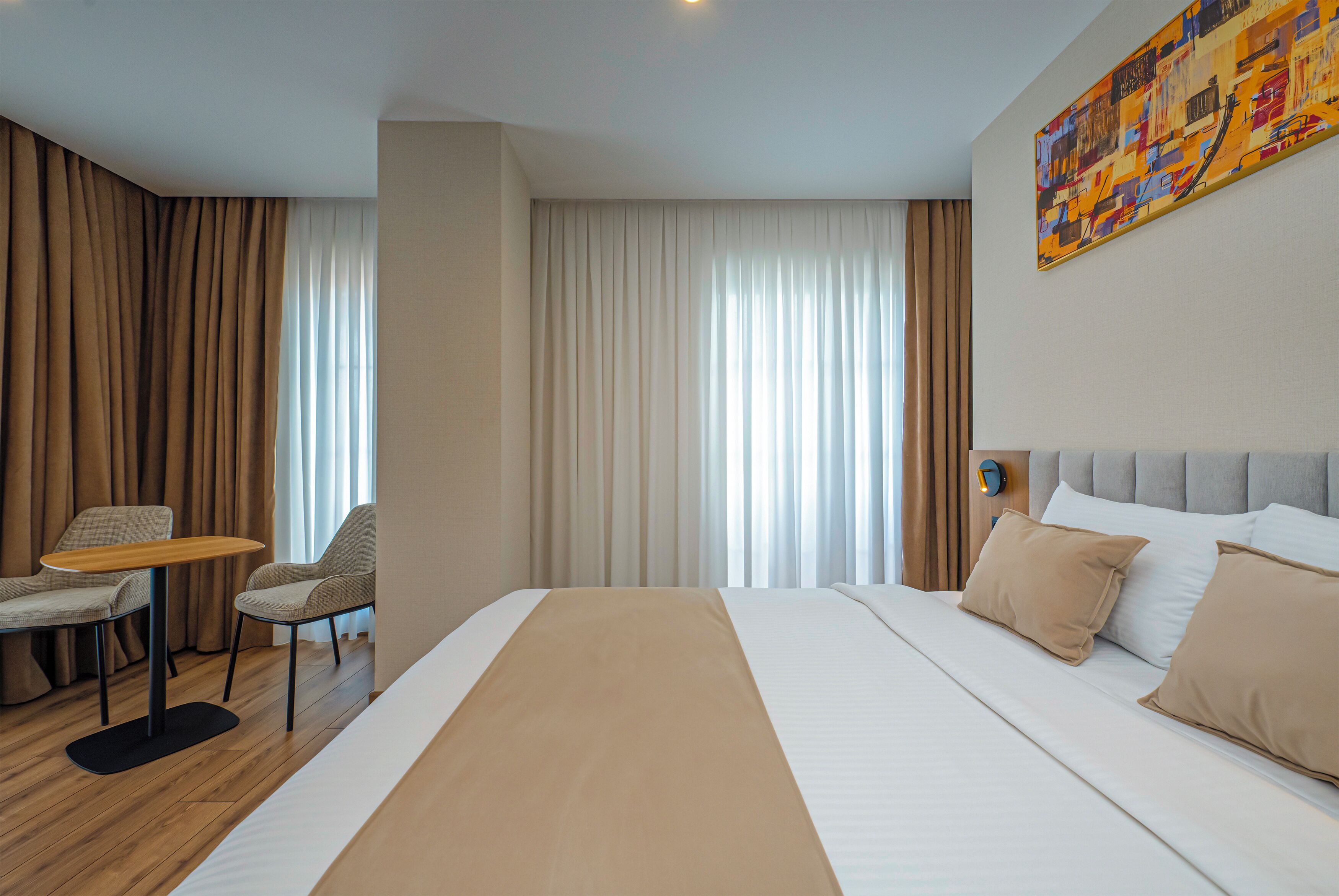 A hotel room with a large bed, a small table, two chairs, a nightstand, and a painting on the wall.