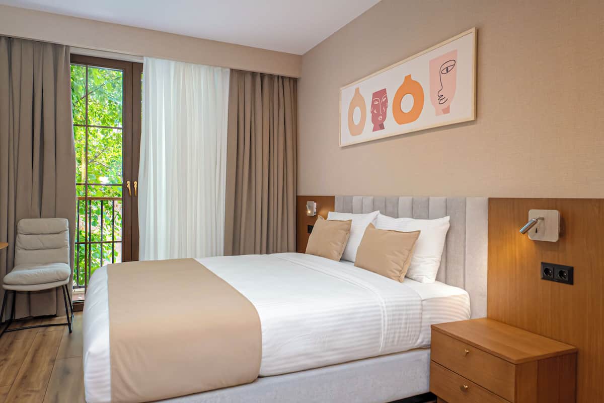 Une chambre d’hôtel avec un grand lit, une table de chevet, une chaise et une fenêtre avec des rideaux.