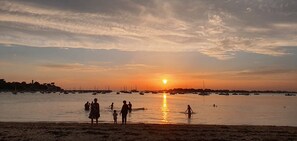 A sunset over a calm sea with boats and people on the shore.