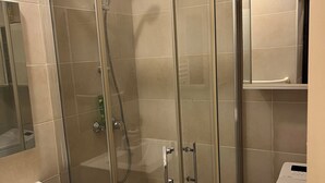 A glass-enclosed shower with a handheld showerhead, a white sink, and a mirror above it. - Charming apartment close to everything (Cavalaire-sur-Mer)