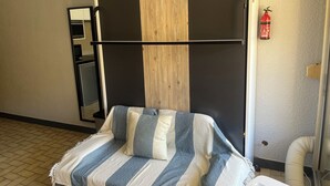 A bedroom with a bed, a wooden wardrobe, a mirror, a fire extinguisher, and a heater. - Charming apartment close to everything (Cavalaire-sur-Mer)