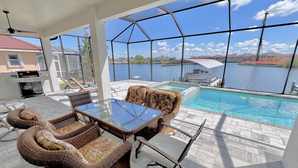 Un espace aménagé au bord de la piscine, avec des meubles en osier, une table en verre et une vue sur un lac.