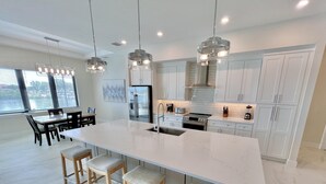 Une cuisine moderne dotée d’un grand îlot central, d’appareils électroménagers en acier inoxydable et de luminaires suspendus.