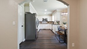 A kitchen with white cabinets, a wooden floor, and a dining area with a bench and table.