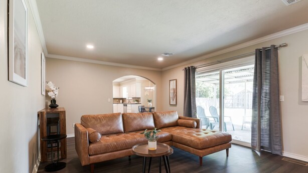 A living room with a brown leather sectional sofa, a small round table with a plant, and a wooden side table.