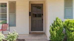 A house with a gray front door, a red chair outside, and green shutters on the windows.