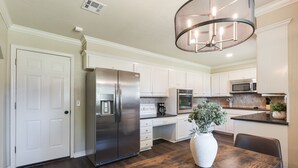 A modern kitchen with white cabinets, stainless steel appliances, and a wooden dining table.