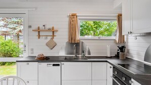 Cozinha moderna com armários brancos, pia de aço inoxidável e janela com cortinas.