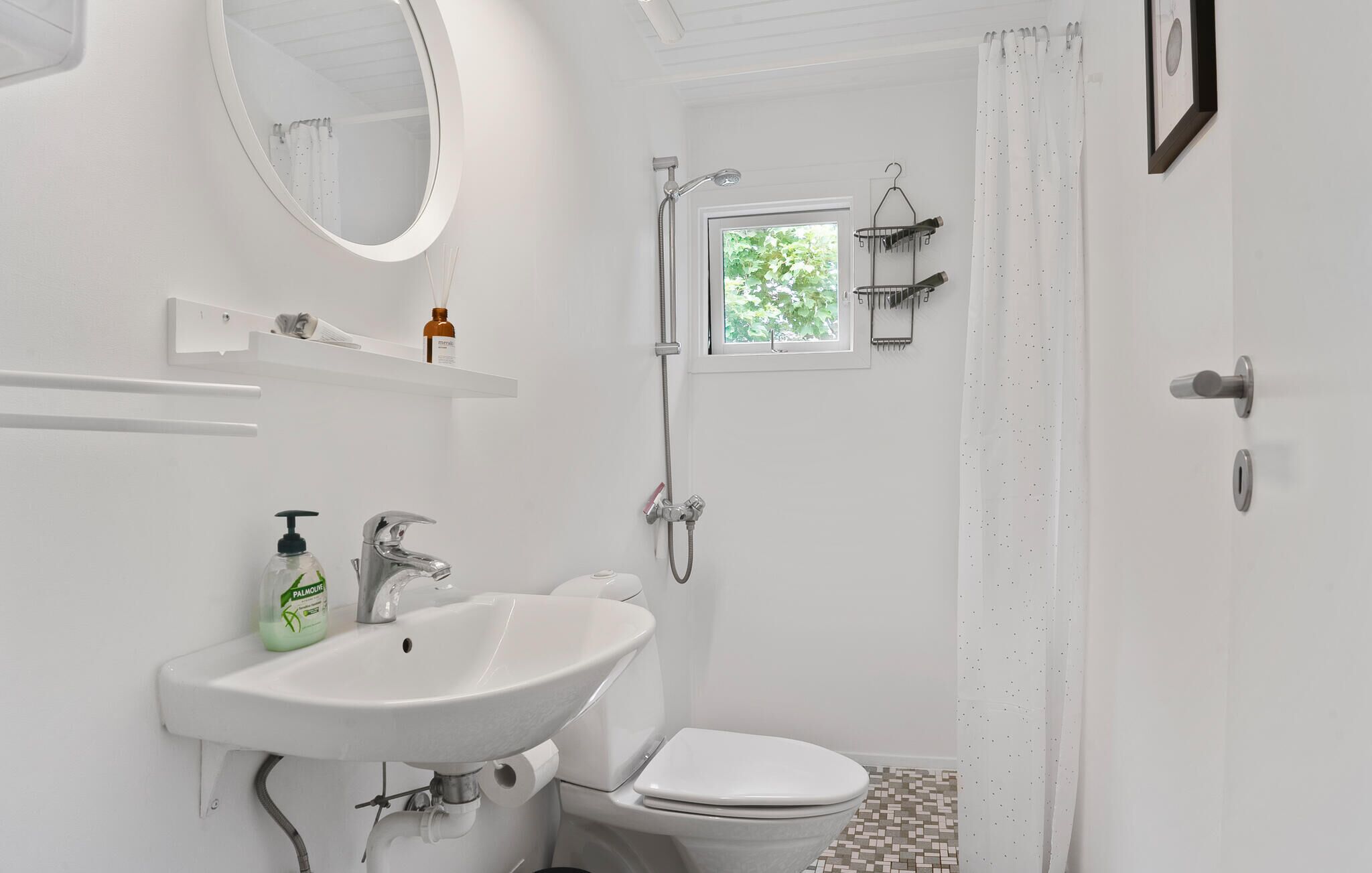 A bathroom with a white sink, toilet, and shower. There is a window above the shower, and a mirror on the wall.
