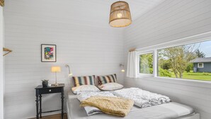 Quarto com cama, mesas de cabeceira, luminária pendente, janela com vista para o exterior e quadro na parede.