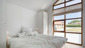 A bedroom with a large window, a bed with a floral quilt, and a view of a building outside. - Beautiful home in Egernsund with sauna (Egernsund)