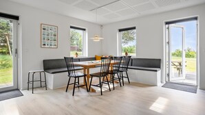 Et moderne spiseområde med et træbord og stole, en siddebænk og store vinduer med udsigt over naturen.