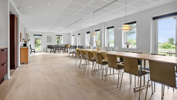 En rummelig spiseafdeling med et langt bord og stole, store vinduer og et loft med et perforeret design.