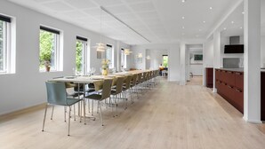 Et moderne spiseområde med et langt bord, stole og hængende lamper.
