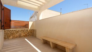 Un balcone con un muro in pietra, una panchina di legno e vista sul cielo.