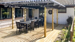 En overdækket terrasse med et bord og stole, en darttavle og en pergola med lyskæder.