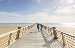 A wooden pier extending towards the beach with a clear sky above.