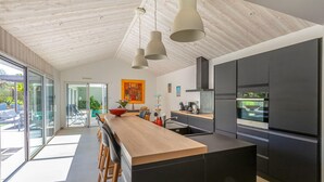Una cocina moderna con una isla de madera, armarios negros y un ventanal grande.