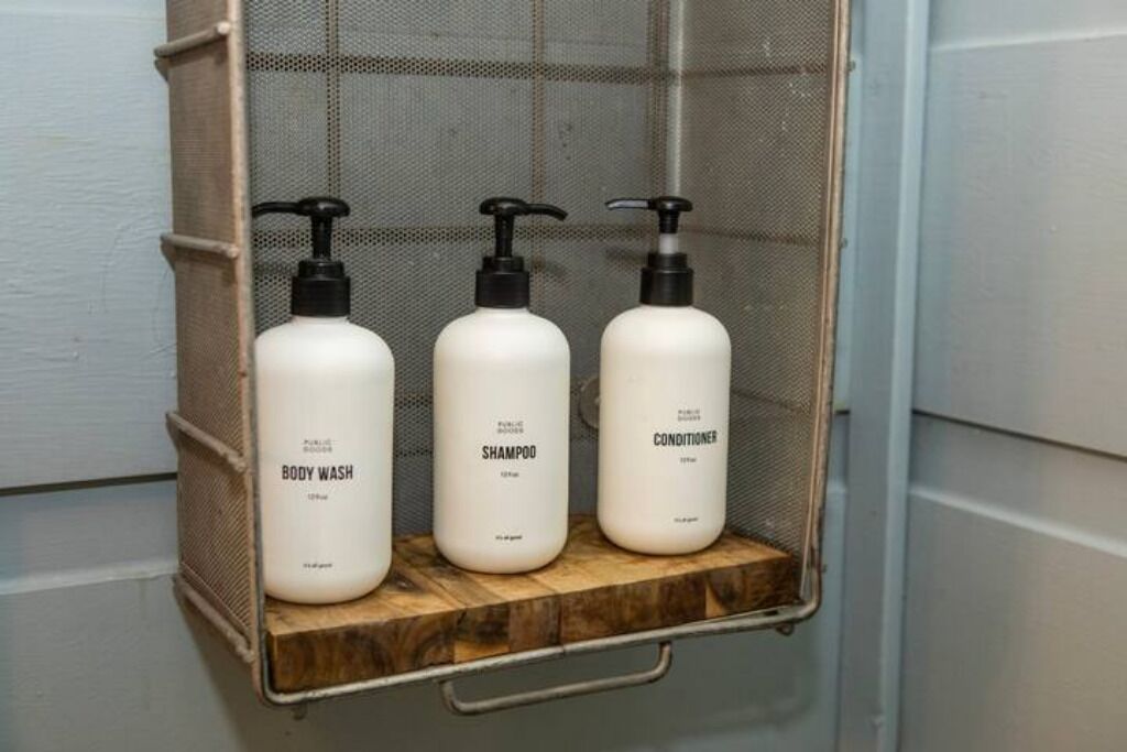 Trois bouteilles de gel douche, de shampoing et d’après-shampoing sur une étagère en bois.