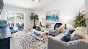 A modern living room with a ceiling fan, a large window, a sofa, a coffee table, and a potted plant. - Spacious Pet-Friendly Beach Home (Cape Canaveral)