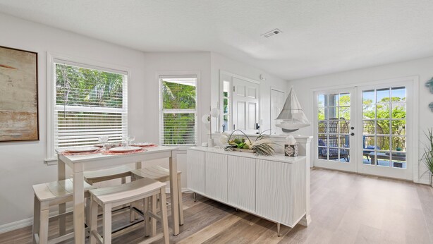 A bright kitchen with white cabinetry, a wooden dining table, and a view of the outdoors through large windows. - Spacious Pet-Friendly Beach Home (Cape Canaveral)