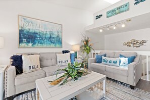 A modern living room with two grey sofas, a white coffee table, and a large abstract painting. - Pet Friendly · Walk to Beach · Rocket Launch View (Cape Canaveral)