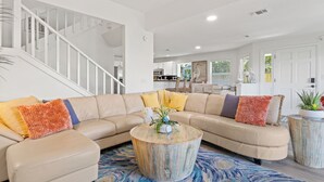 A modern living room with a beige sectional sofa, a round coffee table, and a staircase leading to an upper level. - Spacious Pet-Friendly Beach Home (Cape Canaveral)