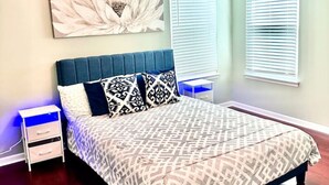 Ein Schlafzimmer mit einem Bett, einem Deckenventilator, einem Nachttisch und einem an der Wand befestigten Kunstwerk.