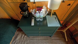 Een kleine kamer met een groene dressoir, een koffiezetapparaat, een lamp en een mand met waterflesjes en een rood zakje.