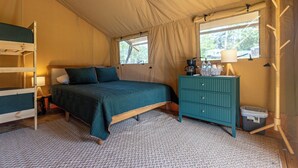 Een tent met stapelbedden, een bed, een dressoir en een raam met uitzicht op bomen.