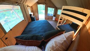 Et teltformet værelse med seng, puder, et lille bord med lampe og vinduer.