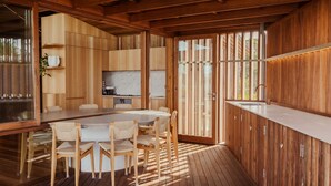 A wooden interior with a dining area, kitchen, and large windows.