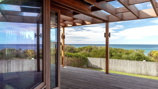 A wooden deck with glass doors leading to a view of the ocean.