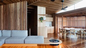 A modern living room with a grey sectional sofa, wooden flooring, a kitchen area with a sink and cabinets, and a dining area with a table and chairs.