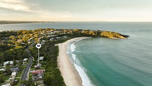 An aerial view of a coastal area with a beach, residential buildings, and a road marked with a 'M' sign.
