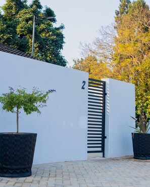 Welcome to a serene entrance with a black gate and beautifully landscaped planters.