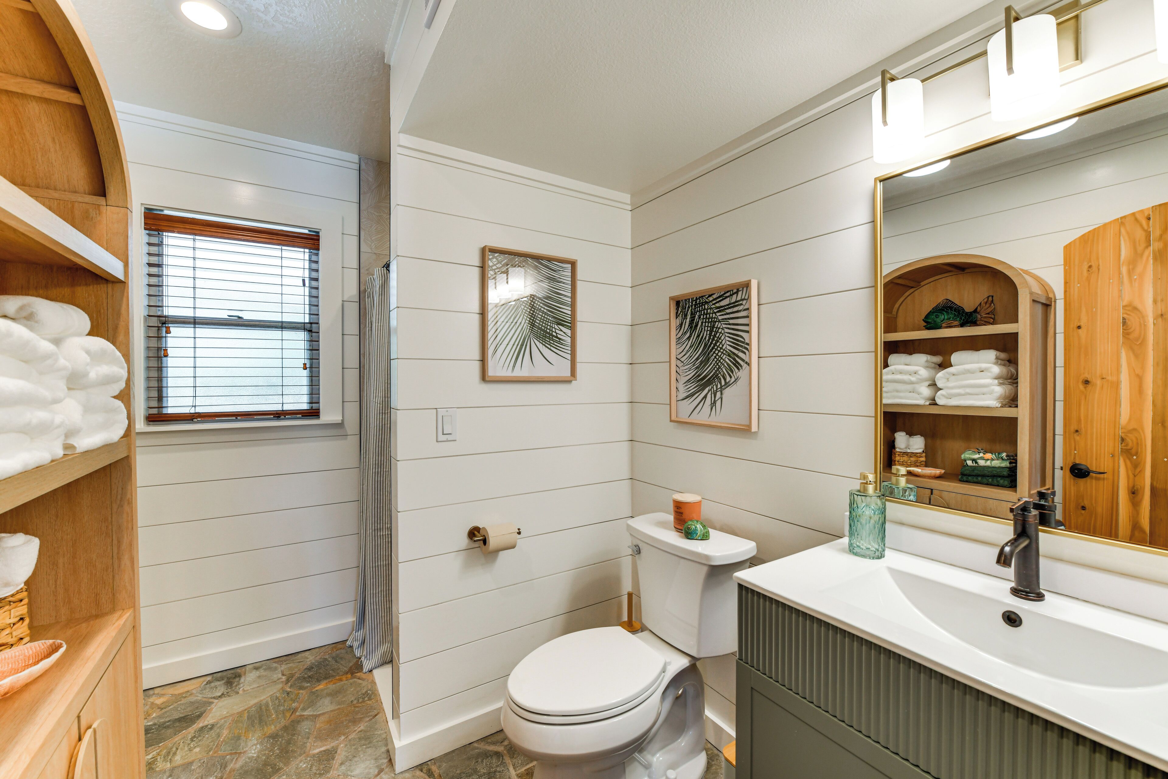 A bathroom with a white toilet, a sink with a mirror, and wooden shelves with towels.