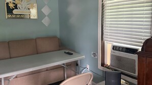 A room with a sofa, a table, a chair, a wall-mounted air conditioner, and a decorative mirror.