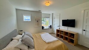 Un dormitorio con cama, televisor, asiento junto a la ventana y un armario de madera.