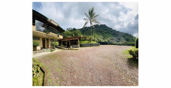 A building with a balcony and a covered outdoor area, surrounded by a gravel driveway and greenery. - Hotel Tapanti Media de Orosi (Orosí)