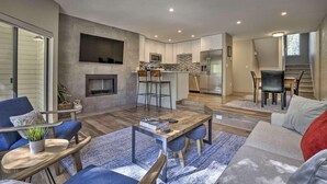 A modern living room with a fireplace, a dining area, and a kitchen with a stone backsplash.