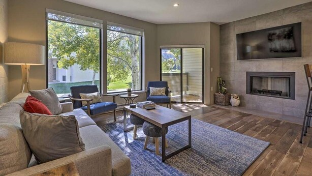 A modern living room with a sofa, chairs, a coffee table, a fireplace, and large windows.