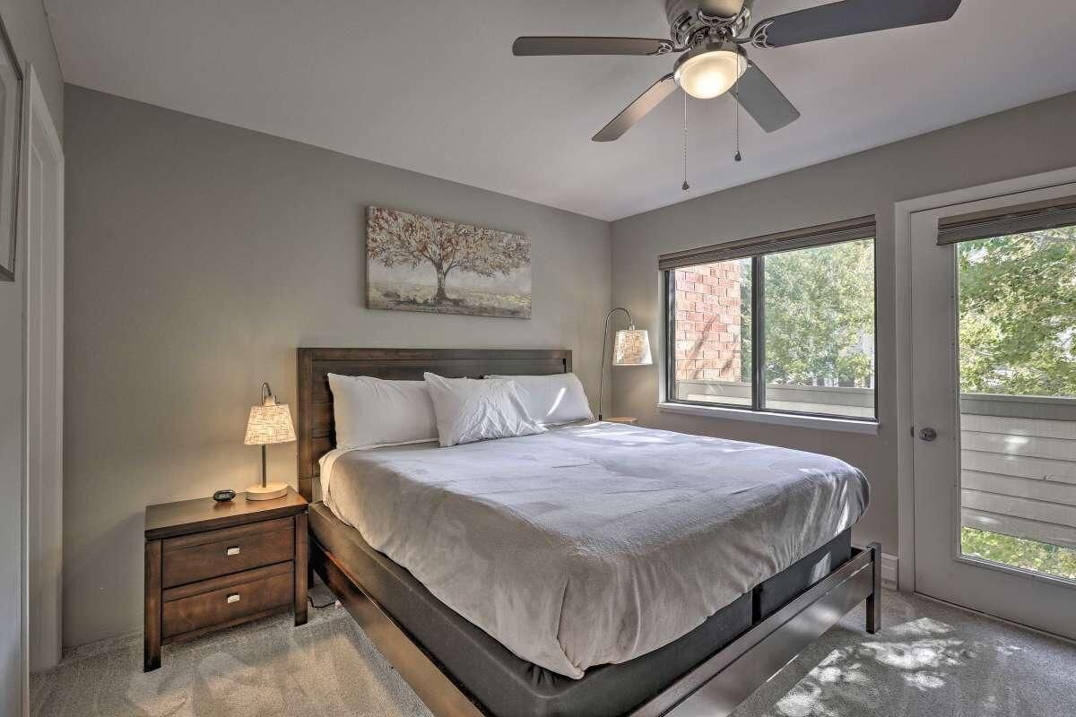 Une chambre à coucher comprenant un lit, une table de chevet, une lampe, un ventilateur de plafond, une fenêtre et des œuvres d’art.