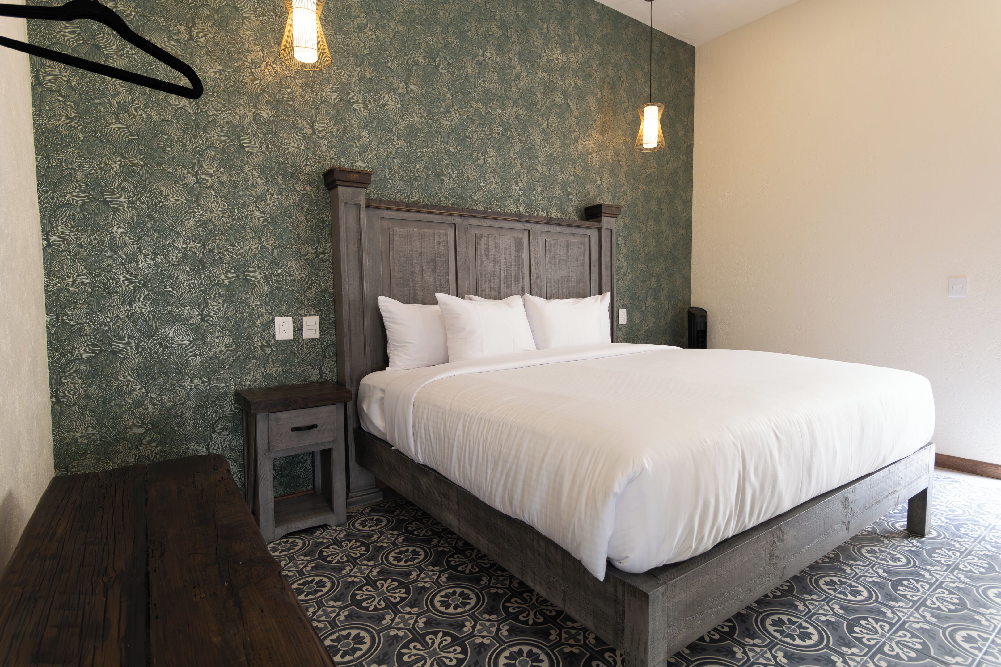 Une chambre avec un grand lit, une tête de lit en bois, des tables de chevet et des carreaux de sol à motifs.