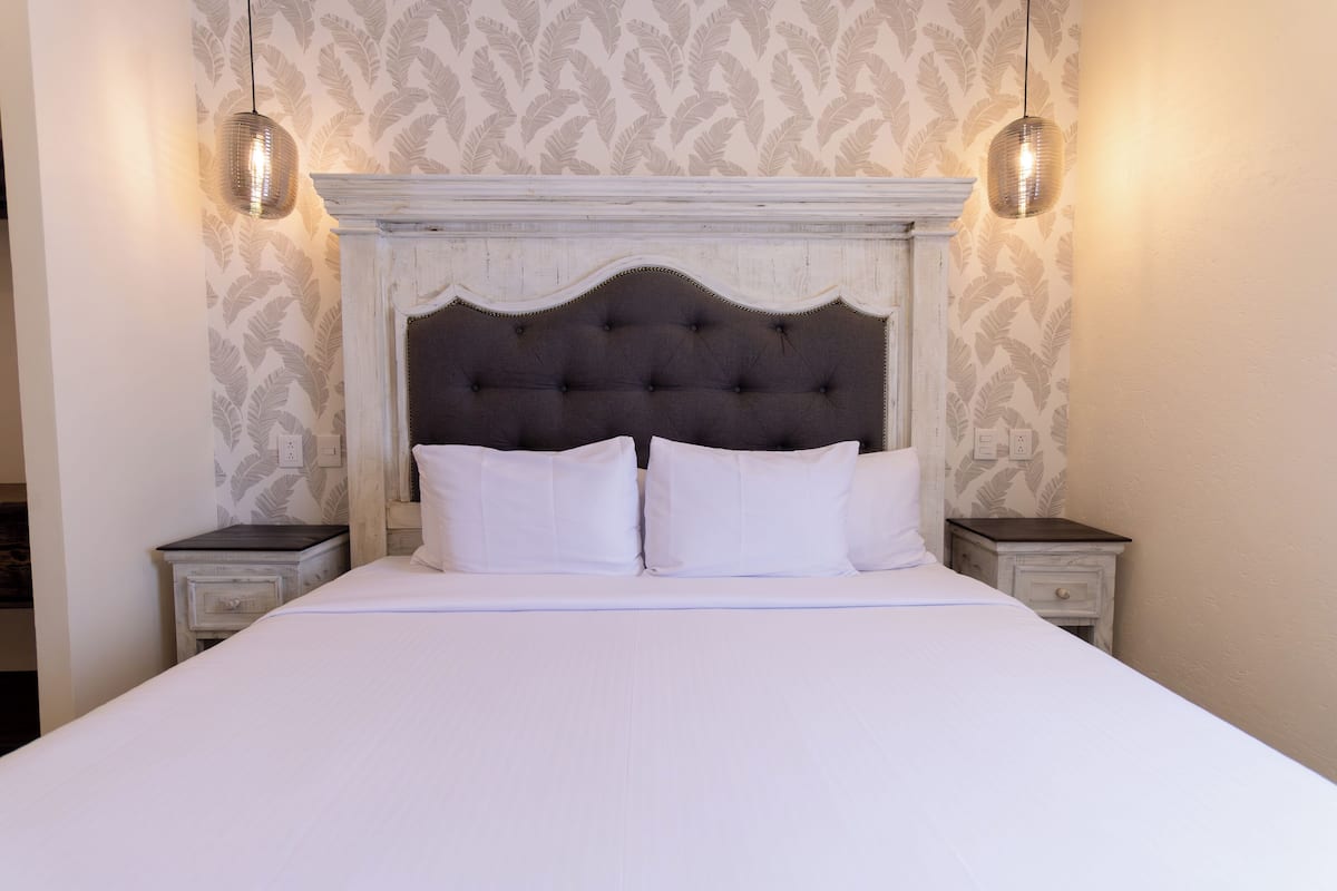 A bed with a tufted headboard, two bedside tables, and patterned wallpaper.